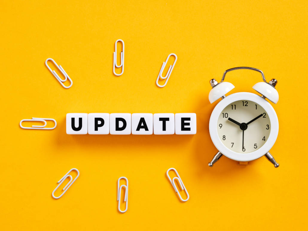 Updatewecker Ein Wecker auf orangefarbenem Hintergrund neben dem Wort „Update“ und kreisförmig verteilten Büroklammern
