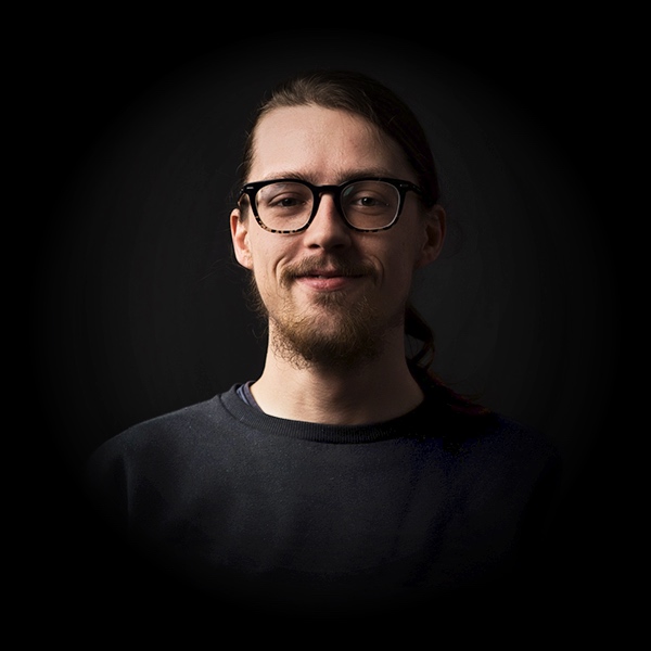 Mann mit Brille und Bart lächelt vor schwarzem Hintergrund.