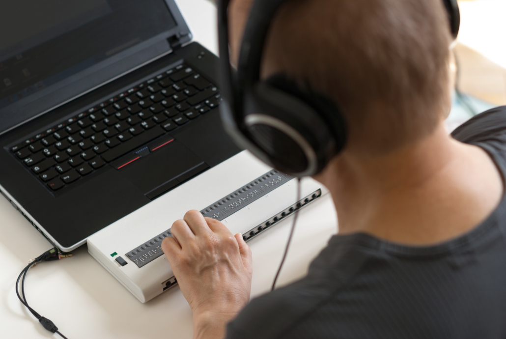 Person nutzt Laptop mit Braillezeile und Kopfhörern für barrierefreies Arbeiten.